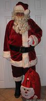 Full front view of Santa suit worn showing coat, pants, hat, wig, beard, belt, boot covers, gloves, and red drawstring bag