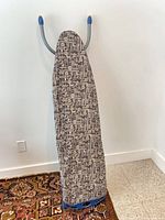 Ironing board folded upright against wall showing patterned cover and blue plastic tip