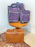 Three purple Tracker suitcases on table, brown Presto leather suitcase below
