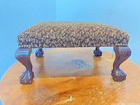 Full view of footstool showing upholstery and carved legs