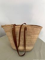 Front view of woven straw tote showing overall shape, straw weave pattern and leather straps