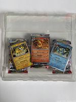 Front view of three cards and booster packs in plastic tray