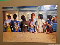 Poster mounted on wall depicting six women with Pink Floyd album art painted on their backs