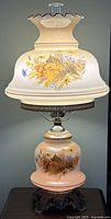 Full view of lamp unlit showing floral globe shade and lower font with metal base