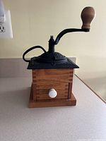Front view of wooden coffee grinder showing crank and closed drawer