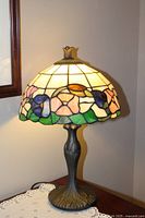 Full view of lamp lit on table showing stained glass shade and metal base