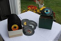 Side view of box of 45s, loose records on table, green case