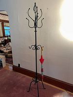 Full view of freestanding wrought iron coat rack with umbrella for scale