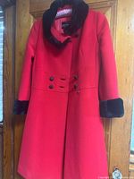 Front view of red wool overcoat hanging, showing black fur collar and cuffs, double-breasted buttons