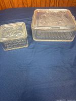 Two clear glass refrigerator dishes with lids on blue cloth