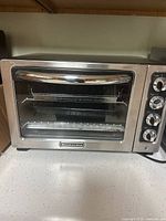 Front view of KitchenAid stainless steel toaster oven with wire rack and perforated tray visible inside