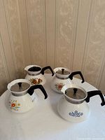 Four Corning Ware tea kettles showing front patterns and lids