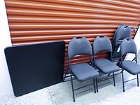 Front view of black square folding card table and three of the upholstered folding chairs