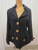 Full front view of black knit coat on mannequin showing wooden buttons, collar, pockets