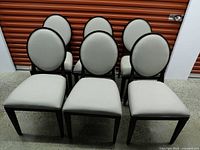 Front view of all six chairs displaying oval backs and light upholstery