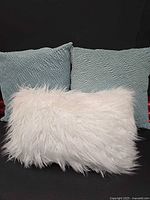 Two light blue square pillows and one white faux fur pillow
