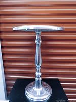 Full side view of chrome-plated round side table showing pedestal and base