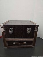 Front view of brown faux leather chest showing latches, drawer and hardware