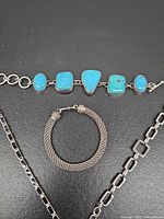 Four sterling silver jewelry pieces laid out: turquoise link bracelet, mesh bangle, black-stone tennis bracelet, rectangular link chain