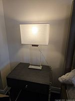 Lit acrylic table lamp on nightstand showing illuminated linen shade and clear base