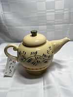 Teapot front showing motif, lid, tag attached