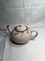 Side view of cream ceramic teapot with vine/leaf pattern