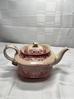 Front view of cream ceramic teapot with red transferware patterns and lid