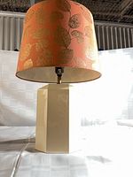 Full view of lamp showing cream ceramic base and coral shade with gold leaf pattern