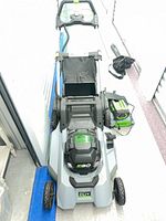 Top view of EGO cordless mower with battery and charger beside it