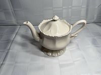 Side view of ivory-cream porcelain teapot showing scalloped base, spout, handle and lid