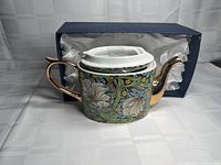 Side view of teapot showing floral design, gold handle and presentation box