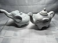Both white ceramic elephant teapots with lids displayed side by side
