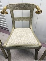 Front view of neoclassical metal dining chair showing ram-head arms, engraved floral frame and upholstered seat