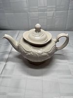 Left side view of ivory ceramic teapot with lid showing embossed scrollwork