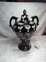Front view of black porcelain urn with lid and brass spigot showing floral enamel