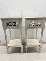 Front view of both matching side tables showing mirrored drawer fronts, turned legs and lower shelves