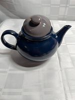 Side view of glossy navy blue stoneware teapot with gray lid, handle left, spout right