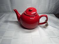 Side view of red stoneware teapot with lid attached tag
