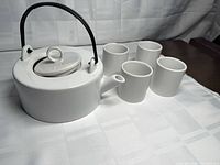 Top angle view of teapot with lid and handle, four cups lined beside it