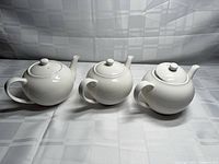 Front view of three identical white ceramic teapots with lids
