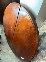 Full view of round/oval wooden tabletop leaning against wall, showing overall wood grain and central seam