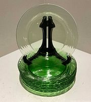 Stack of eight green glass plates with one displayed upright on stand