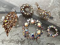 Five gold-tone brooches with aurora borealis stones on wood background