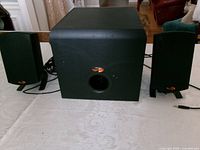Front view of subwoofer flanked by both satellite speakers, showing cables