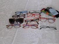 All ten pairs of glasses laid out with two soft cases and cloth visible