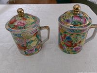 Two porcelain lidded tea mugs side by side showing pattern and gold finials