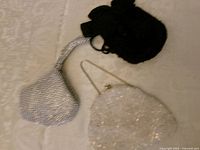 All three purses displayed: black, silver wristlet, white clutch