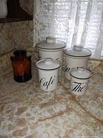 Group shot of four script ceramic canisters with lids and brown glazed pottery jar