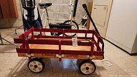 Side view of wooden wagon showing red rails, wheels, logo, handle upright