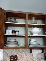Cabinet interior showing tureen, stacks of Corelle plates and bowls, clear glass serving pieces, mugs